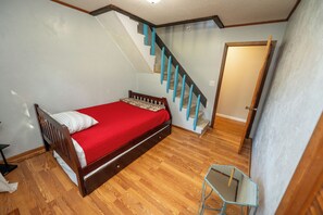 A bedroom with a wooden bed, a red bedspread, a wooden chair, and a staircase with blue railings. - Watts Bar Lake House Retreat (Kingston)