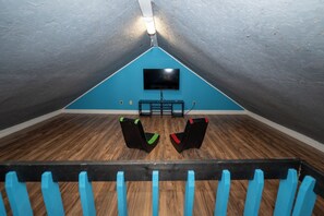 An attic room with a flat-screen TV mounted on the wall, two black chairs with red accents, and a wooden floor. - Watts Bar Lake House Retreat (Kingston)