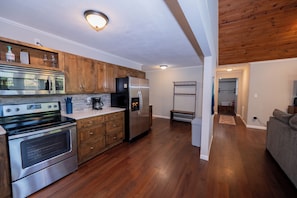 A modern kitchen with stainless steel appliances, wooden cabinets, and a stone backsplash. - Watts Bar Lake House Retreat (Kingston)