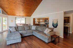 A spacious living room with a large L-shaped sectional sofa, wooden flooring, and a high ceiling with exposed beams. - Watts Bar Lake House Retreat (Kingston)
