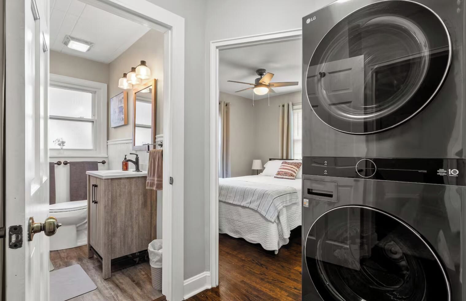 Ein Waschraum mit einer großen Waschmaschine und einem Trockner, ein Badezimmer mit Toilette, Waschbecken und Waschtisch sowie ein Schlafzimmer mit Bett und Deckenventilator.