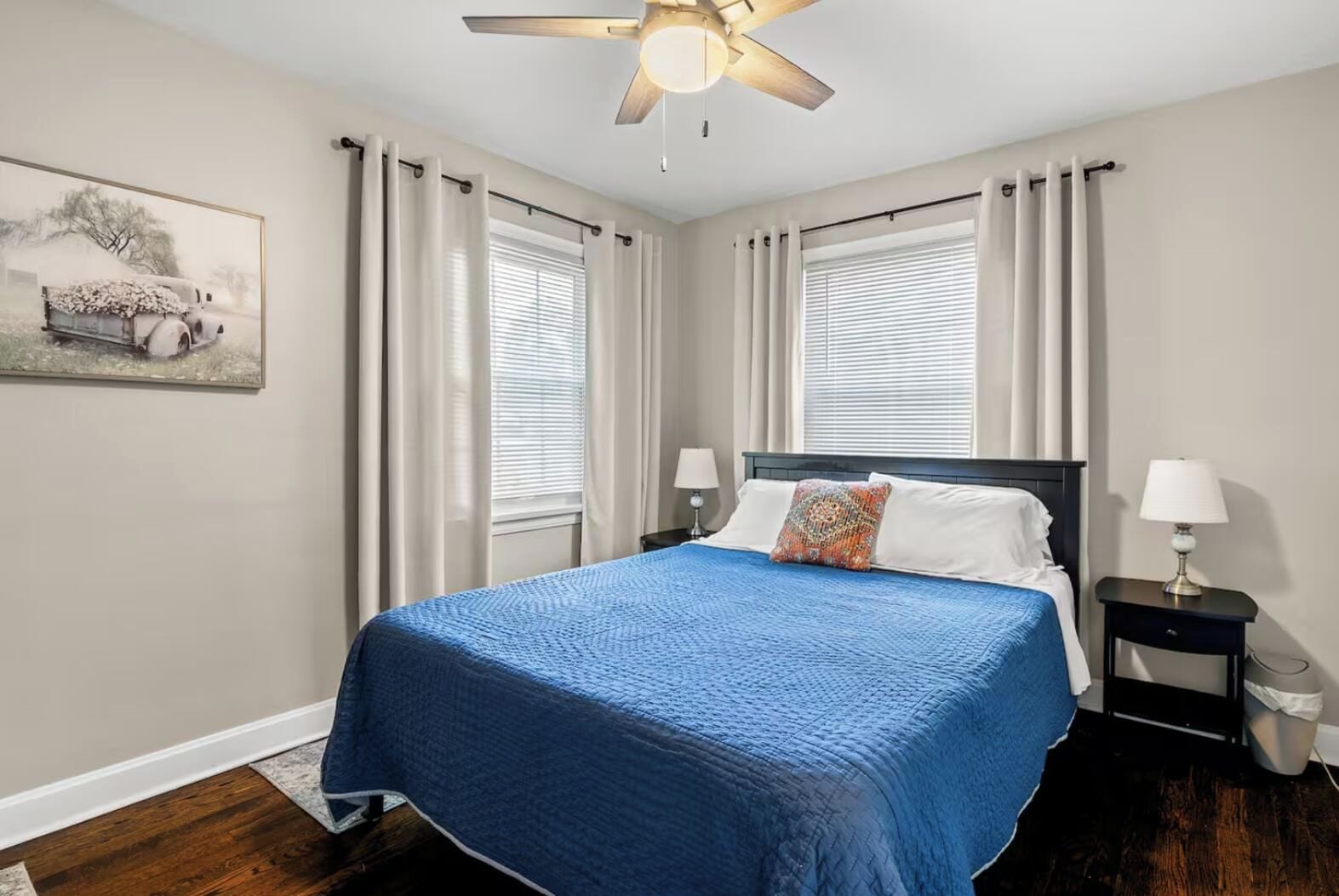 Une chambre à coucher avec un lit, deux tables de chevet, un ventilateur de plafond et une fenêtre avec des rideaux.