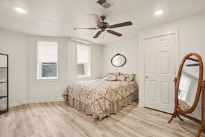 Un dormitorio con cama, ventilador de techo, puerta y ventana.