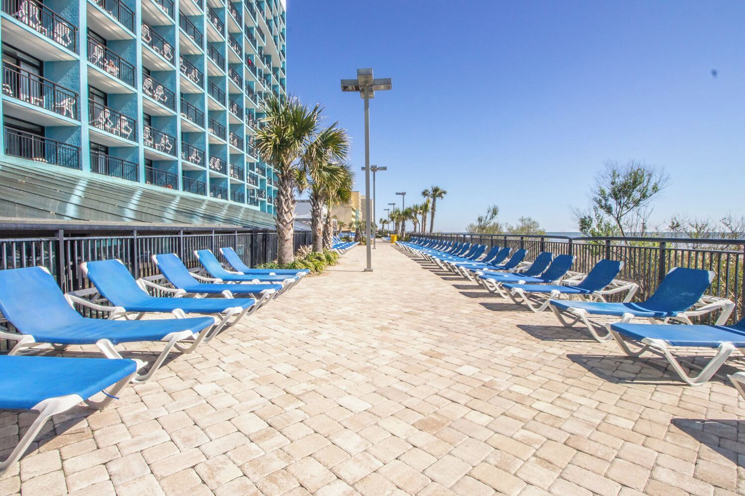 A hotel corridor with rows of blue lounge chairs, a tiled floor, and a building with balconies.