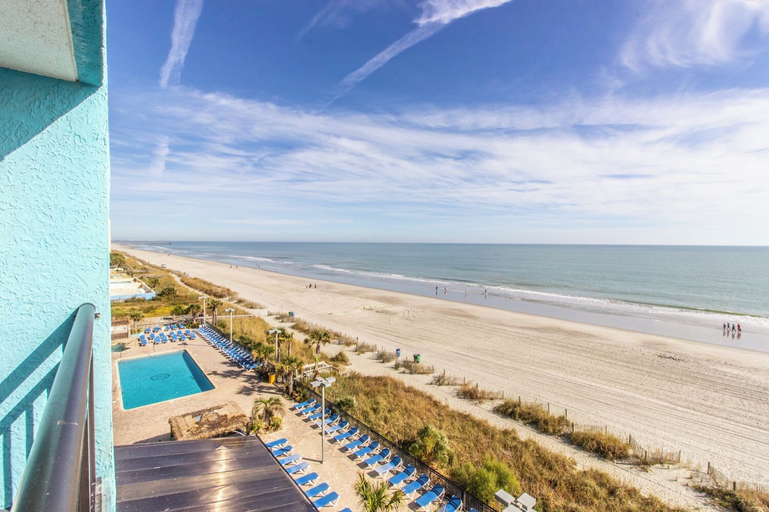 Blick auf den Strand vom Balkon aus, mit Pool und Liegestühlen.