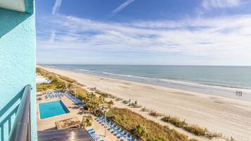 Blick auf den Strand vom Balkon aus, mit Pool und Liegestühlen.