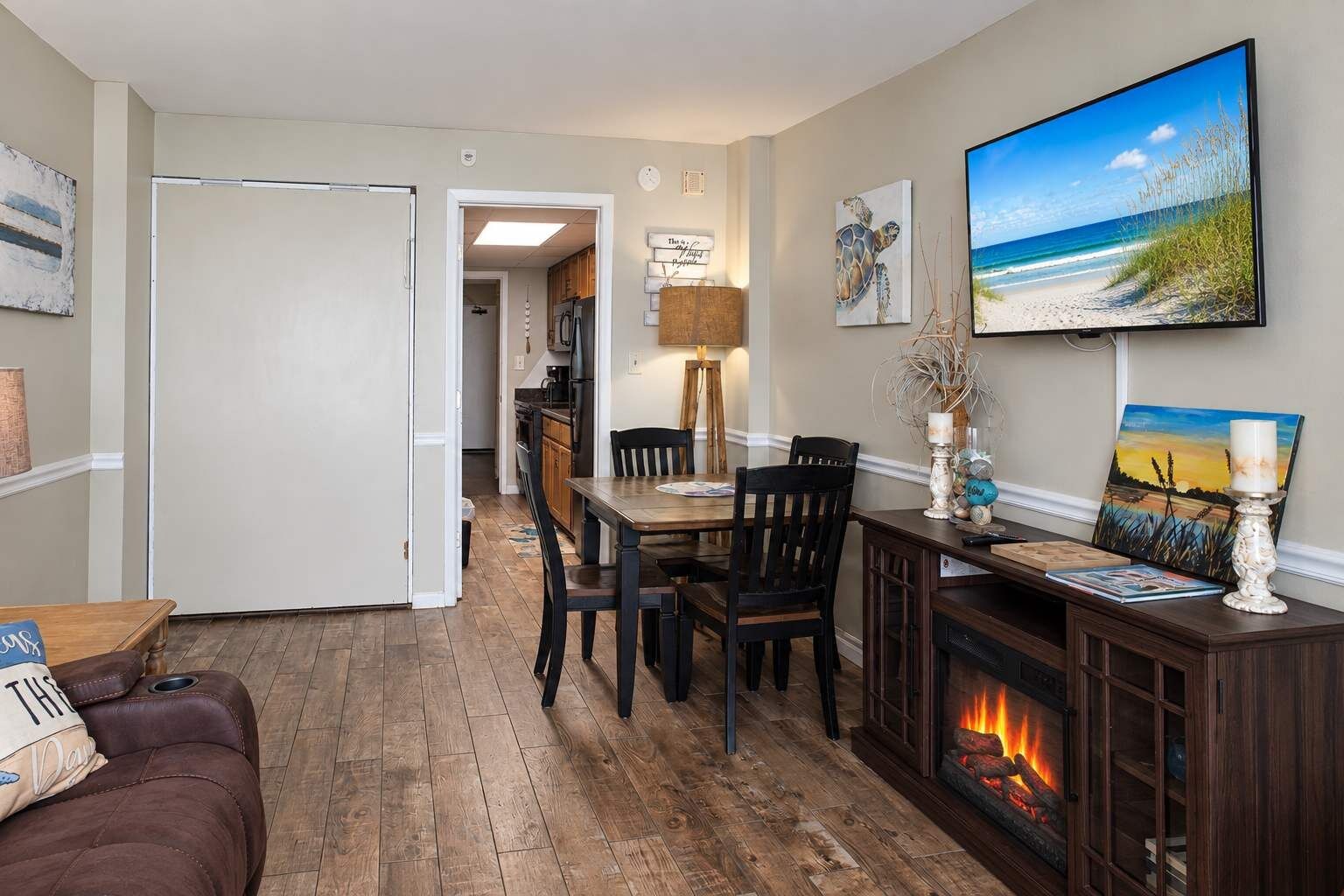 A living room with a fireplace, a dining area with a table and chairs, and a kitchen in the background.