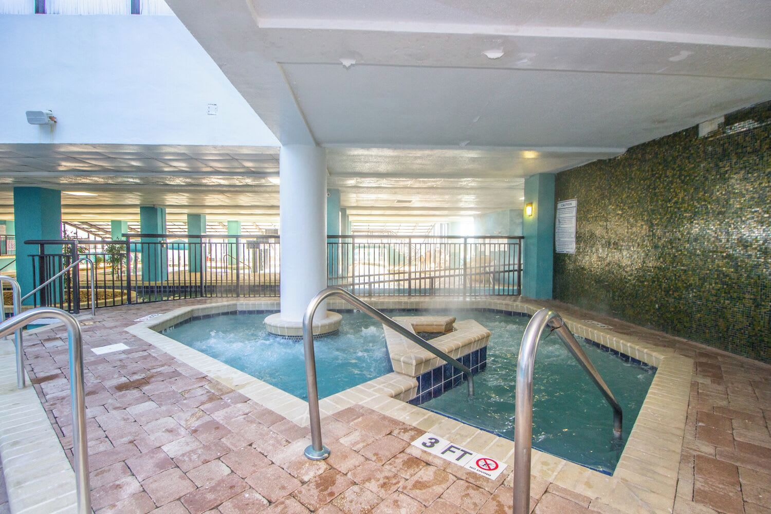 Un espace dédié aux bains à remous, doté d’un sol carrelé, de rampes en métal et d’un panneau indiquant une zone de 90 cm (3 pieds) où il est interdit de plonger.