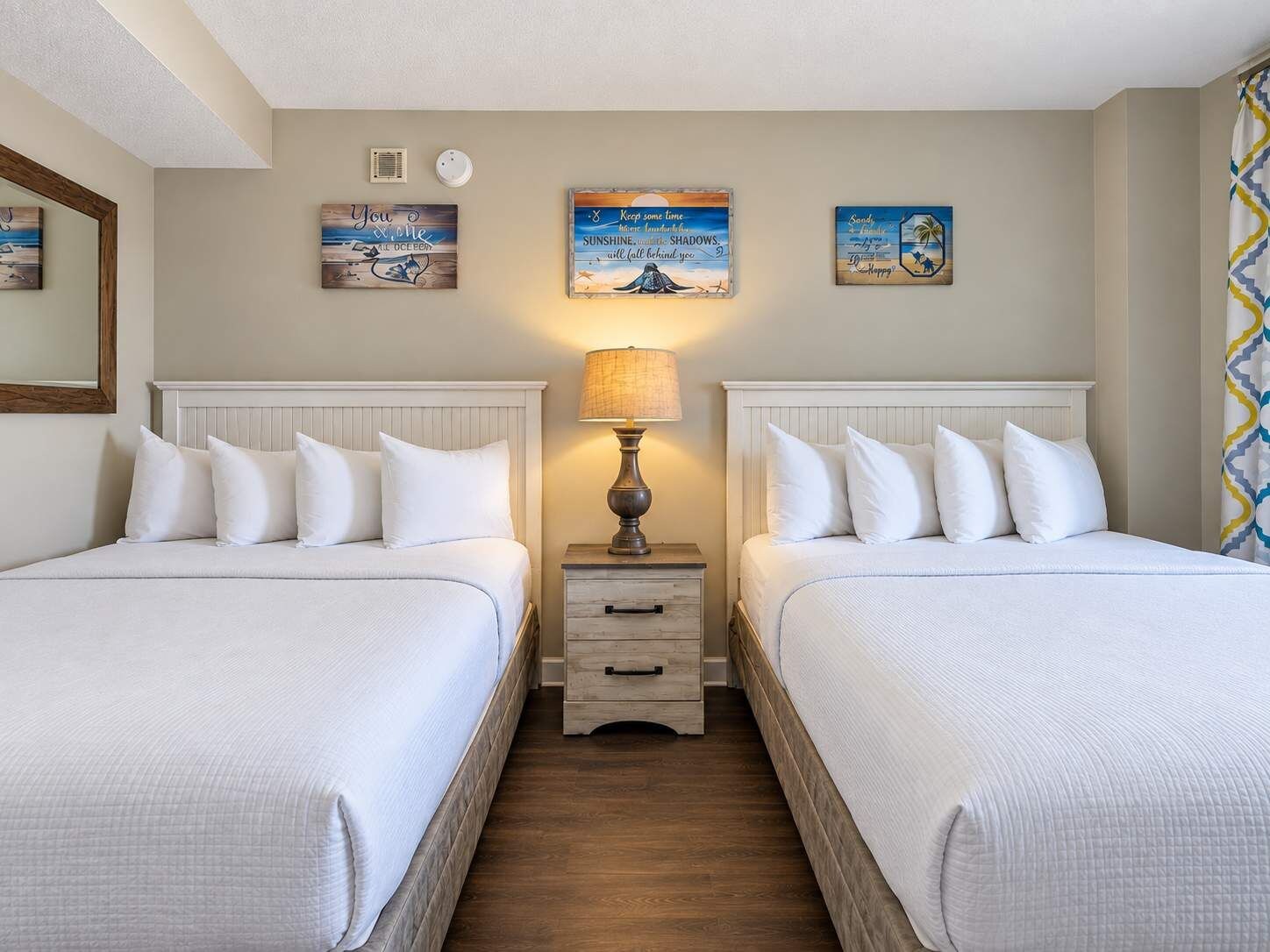 Ein Hotelzimmer mit zwei Betten, einem Nachttisch mit Lampe und Wandbildern.