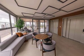 A modern interior with a sofa, chairs, a round table, and large windows offering a view of the city. - Apartamento em Moema com varanda e vista da cidade (São Paulo)