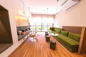 A modern lounge area with a green sofa, round tables, and a laptop on a bench. - Apartamento em Moema com varanda e vista da cidade (São Paulo)