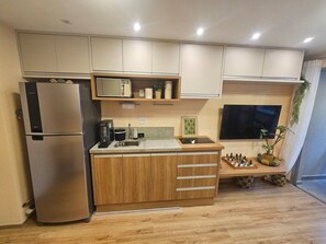 A modern kitchen with a built-in refrigerator, wooden cabinets, a sink, and a flat-screen TV mounted above the counter. - Apartamento em Moema com varanda e vista da cidade (São Paulo)