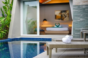 A modern hotel room with a glass wall, a bed, a chair, and a pool.