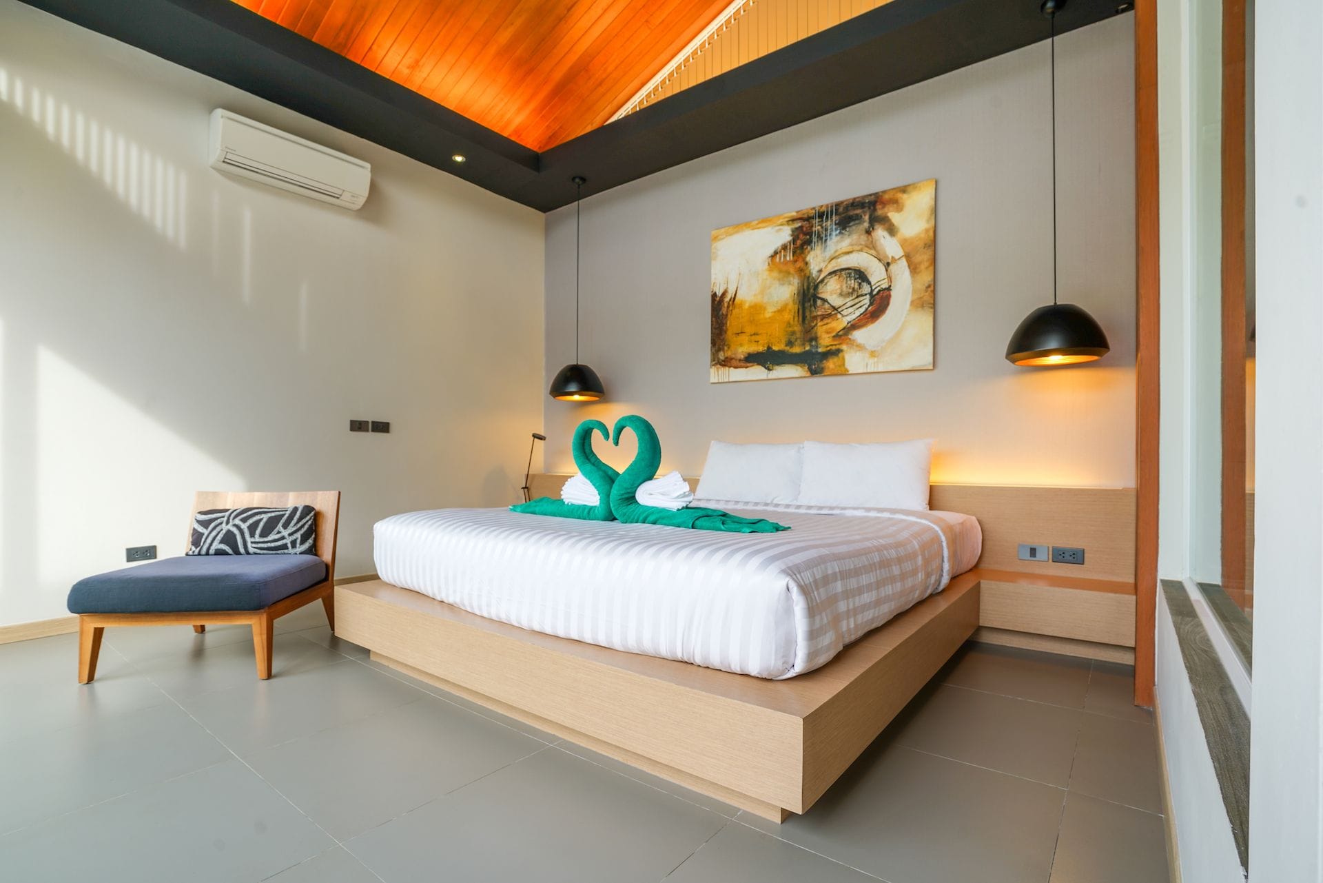 A modern bedroom with a large bed, a bedside table, a chair, and a painting on the wall.