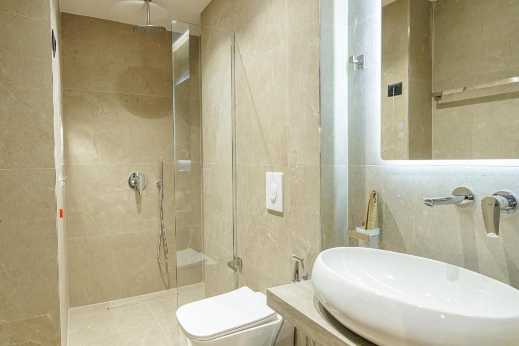 Un baño moderno con ducha envuelta en vidrio, un lavamanos blanco y un espejo grande.