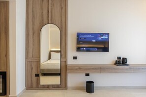 Una camera d'albergo moderna con un ampio specchio, una televisione a schermo piatto fissata al muro, un comodino con una macchina da caffè e un cestino.