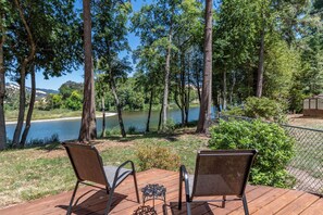 A deck with two chairs and a small table, overlooking a lake with trees and a distant view of hills.