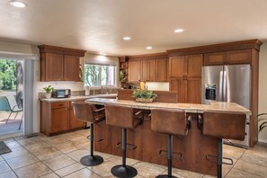 Una cocina con armarios de madera, un refrigerador de acero inoxidable, una zona de bar con taburetes y una ventana que ofrece vistas al exterior.