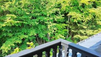 A wooden deck with a wicker chair, surrounded by lush green trees.