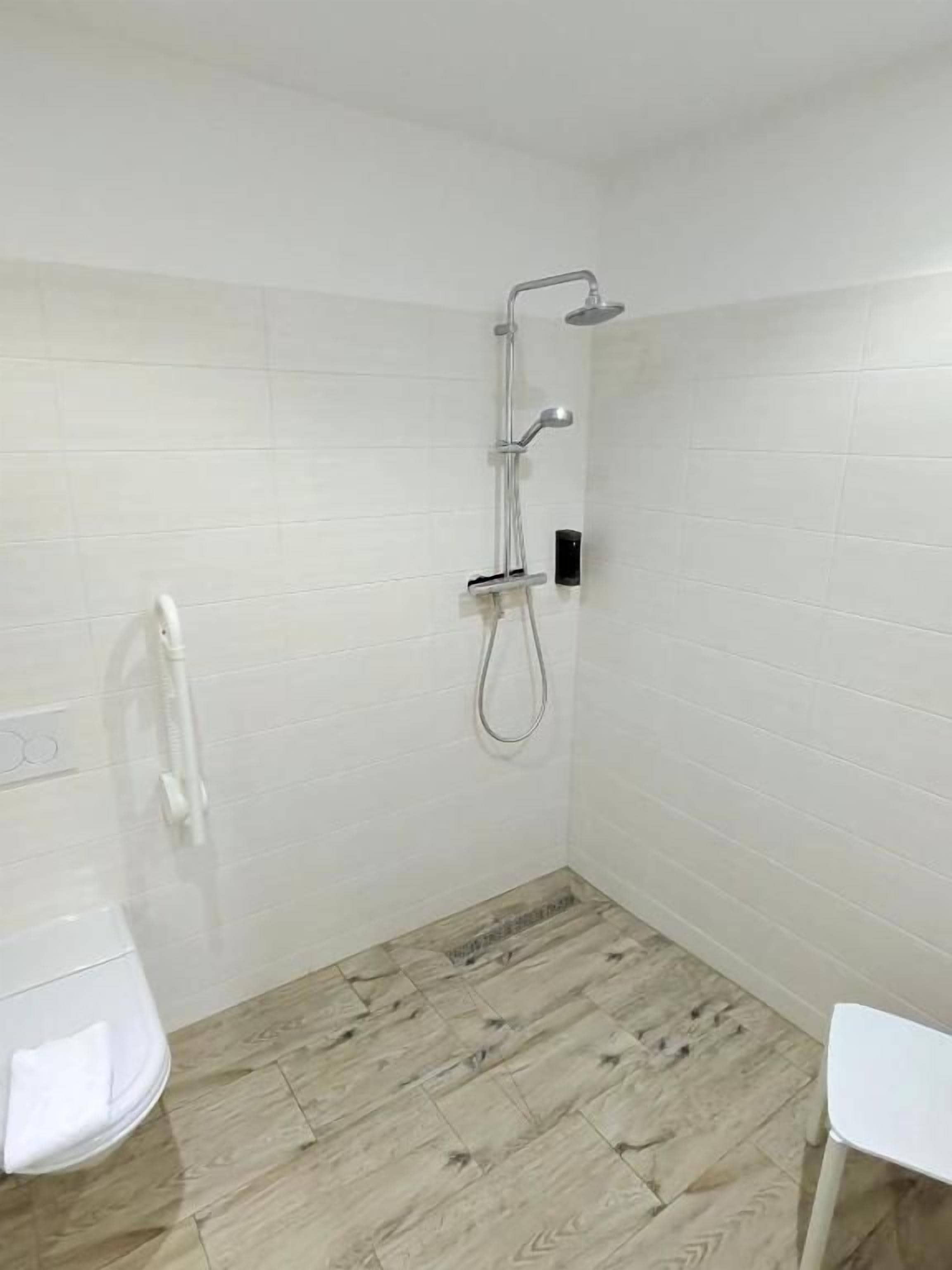 Et badeværelse med bruser, toilet og en hvid stol.