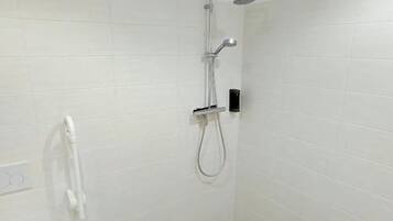Et badeværelse med bruser, toilet og en hvid stol.