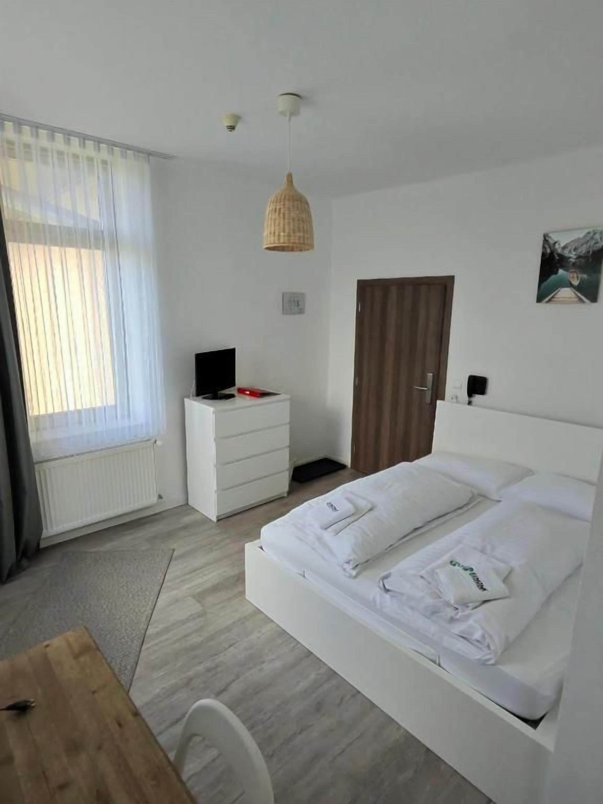 Una camera d'albergo con un letto, una scrivania, una sedia, un comò, una televisione e una finestra con tende.
