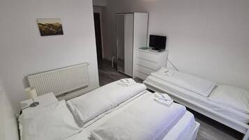 A hotel room with two beds, a wardrobe, a television, and a radiator.