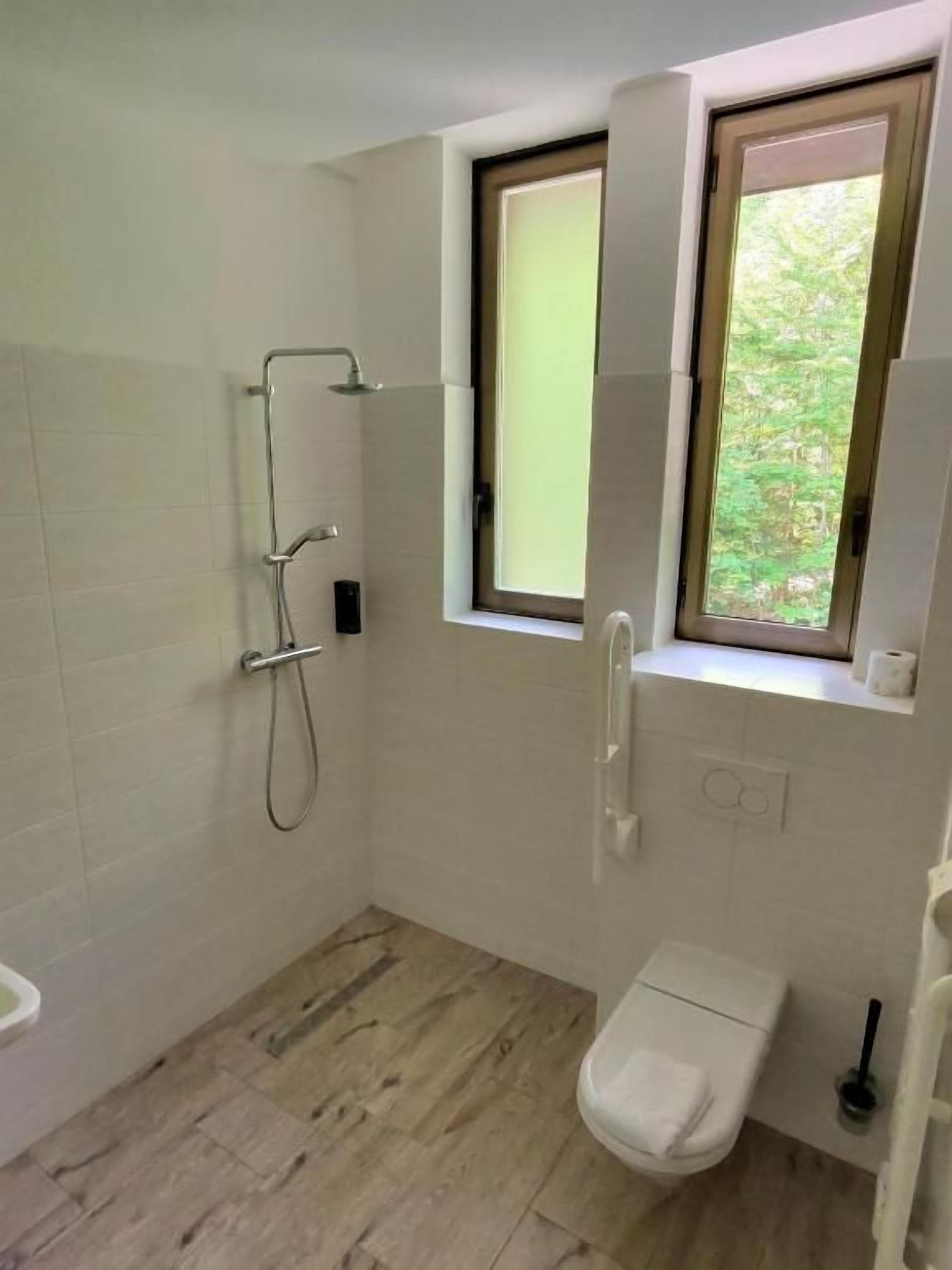 Un baño con ducha, inodoro y ventana con vista a zonas verdes.