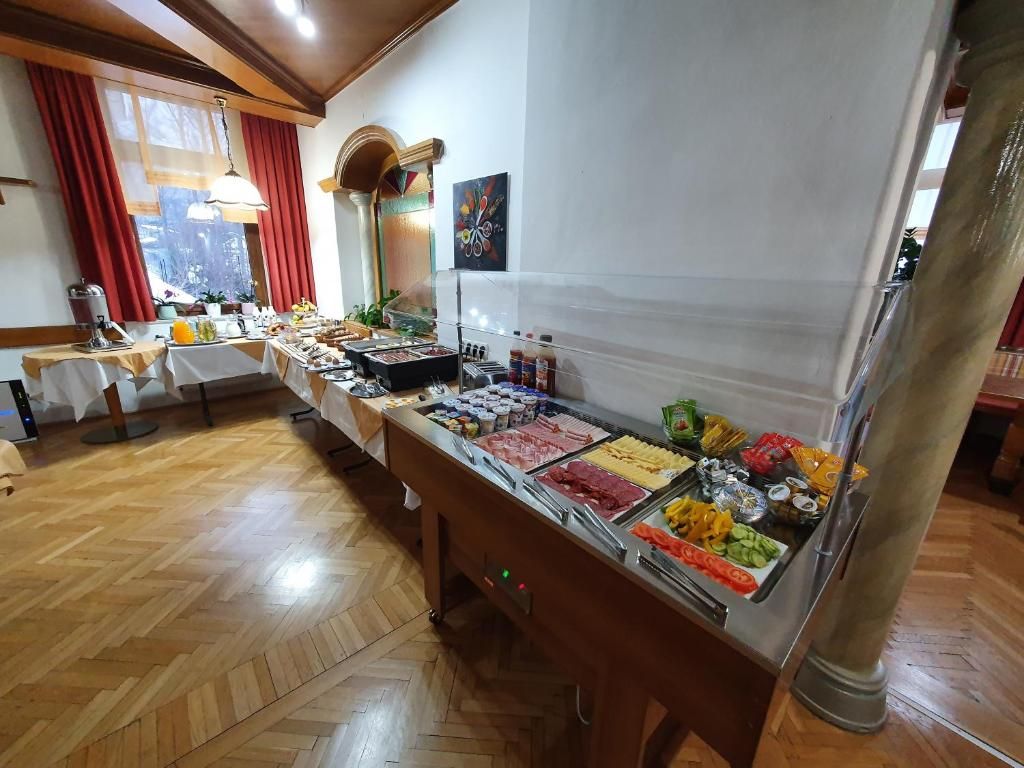 Un bufé con diversos alimentos, piso de madera y una ventana con cortinas rojas.