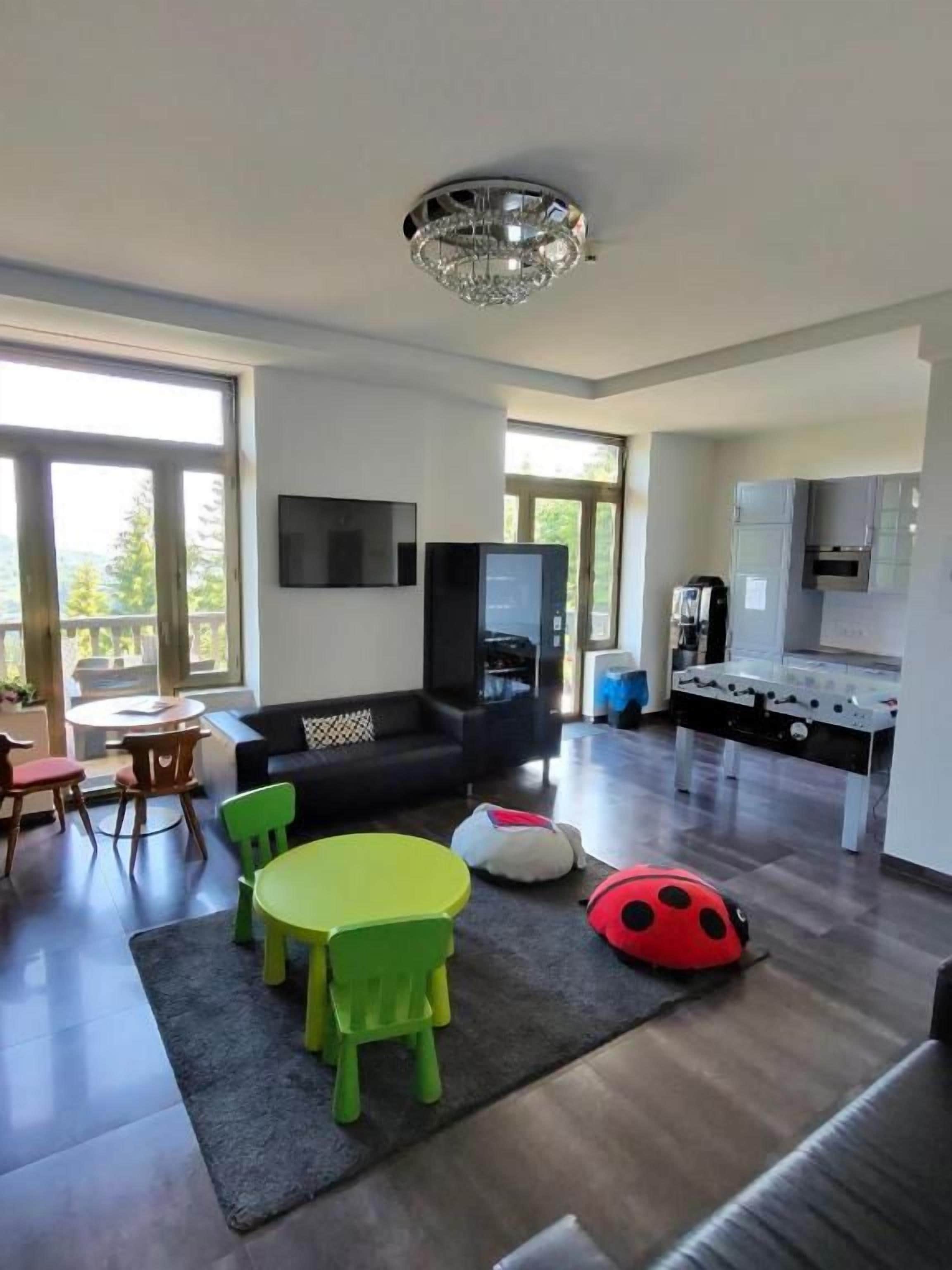 Una sala moderna con un sofá, sillas verdes, una mesa redonda y un sillón de peluche rojo.