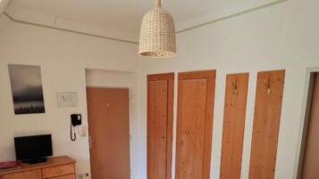 Un dormitorio con cama, armario de madera, escritorio con silla, lámpara colgante y puerta que da a otra habitación.