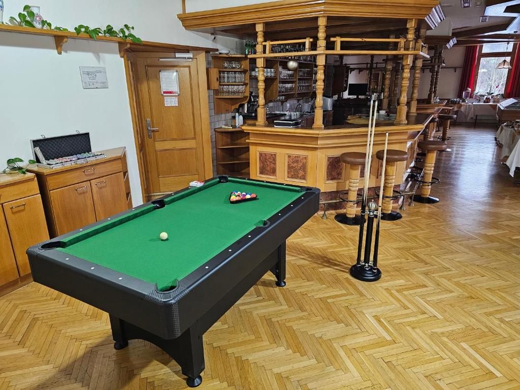 Una mesa de billar con superficie de fieltro verde, armarios de madera y una zona de bar con taburetes.