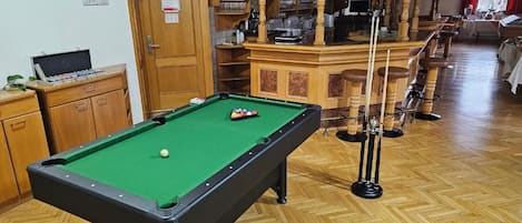 A pool table with a green felt surface, wooden cabinets, and a bar area with stools.