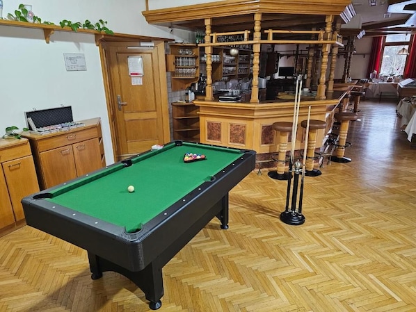 A pool table with a green felt surface, wooden cabinets, and a bar area with stools.