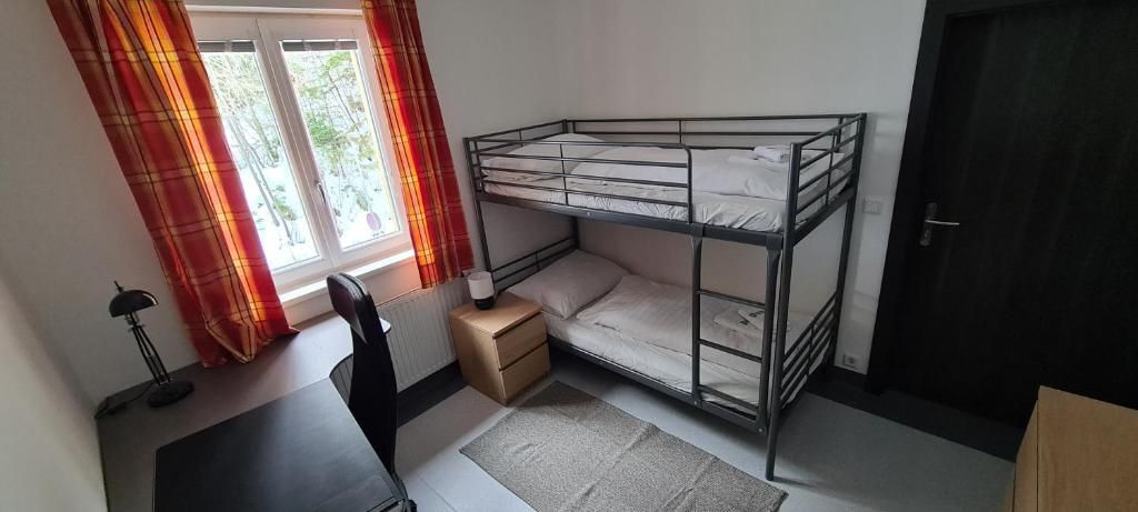 Um quarto com beliche, escrivaninha, cadeira, radiador e janela com cortinas.