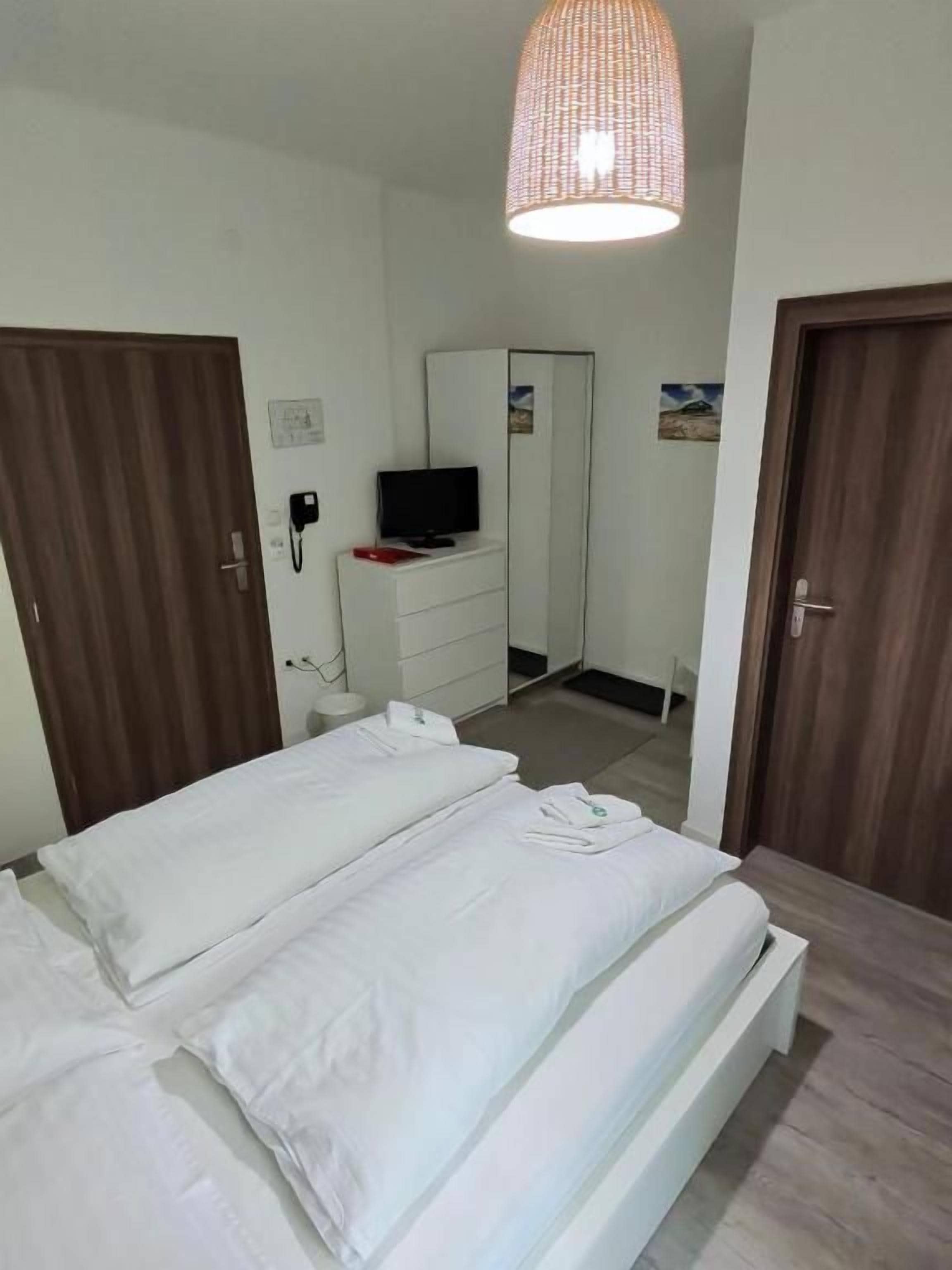 Ein Hotelzimmer mit zwei Betten, einem Kleiderschrank, einem Spiegel, einem Fernseher und einer Hängelampe.
