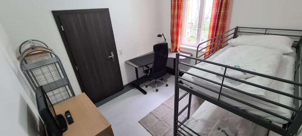 A dormitory room with a bunk bed, a desk with a chair, a wardrobe, and a window with curtains.