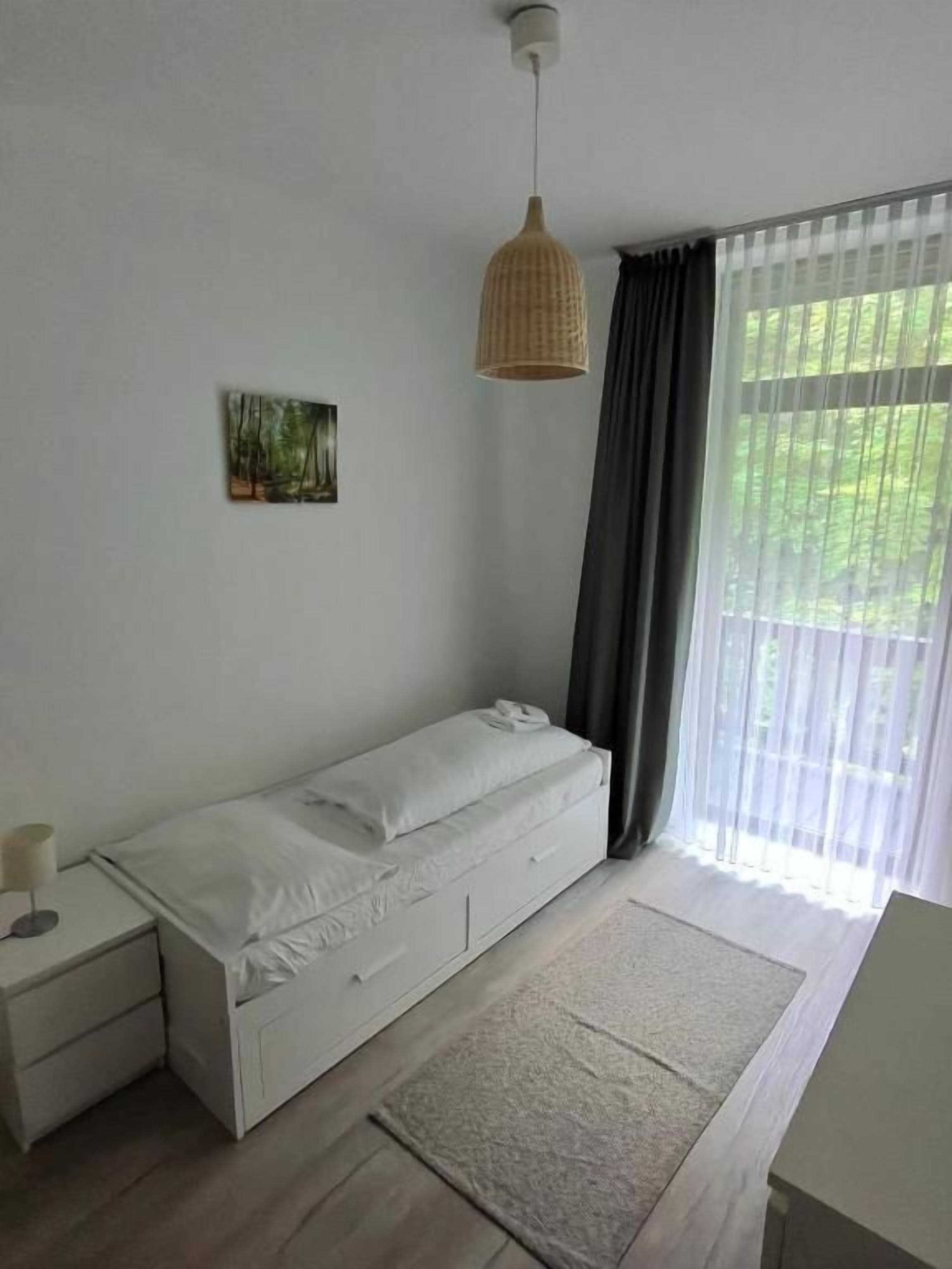 Un dormitorio minimalista con una cama individual, mesita de noche y una lámpara colgante.