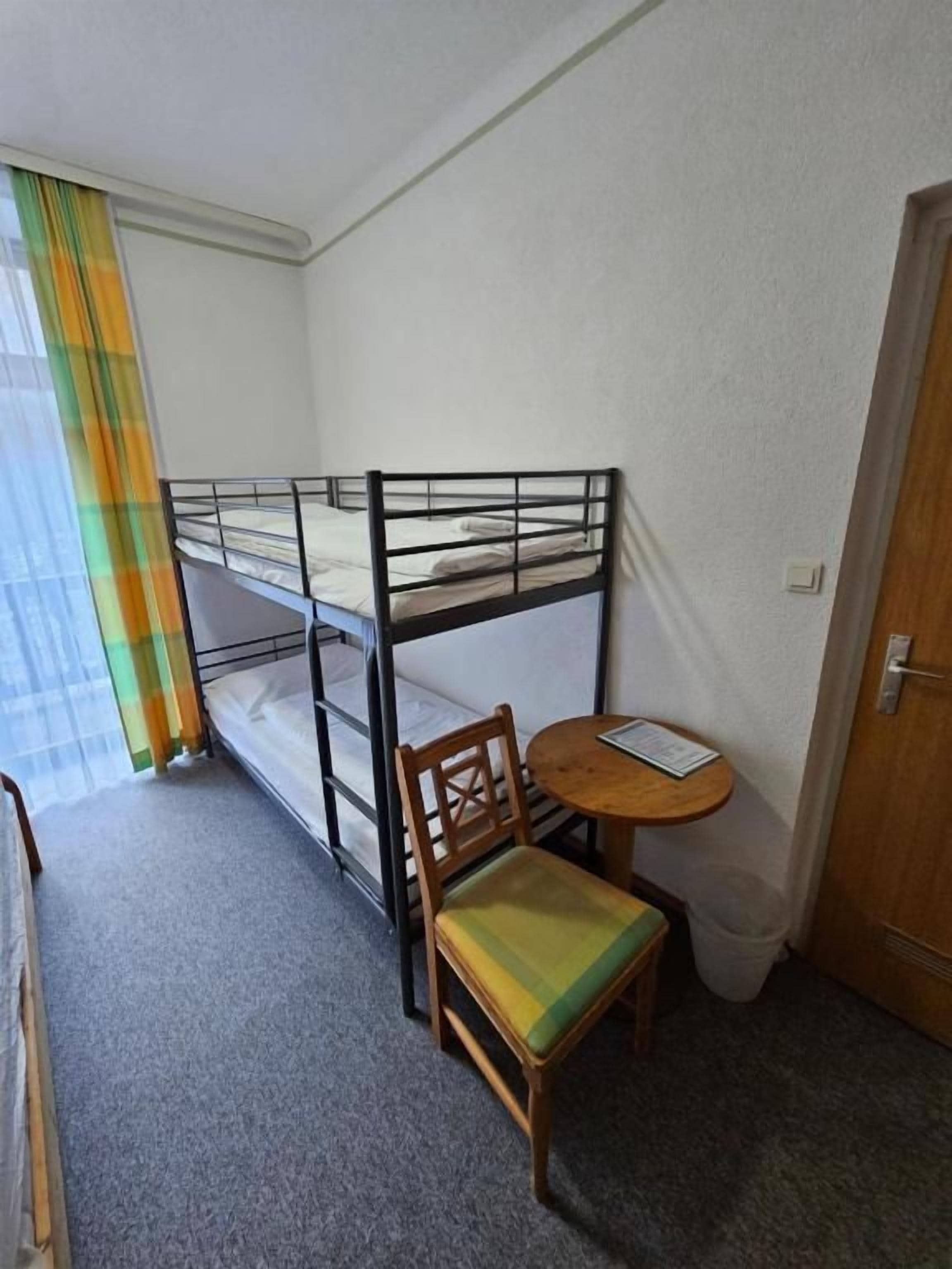 Een kleine kamer met stapelbedden, een enkele stoel, een tafeltje en een deur.