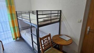 Een kleine kamer met stapelbedden, een enkele stoel, een tafeltje en een deur.