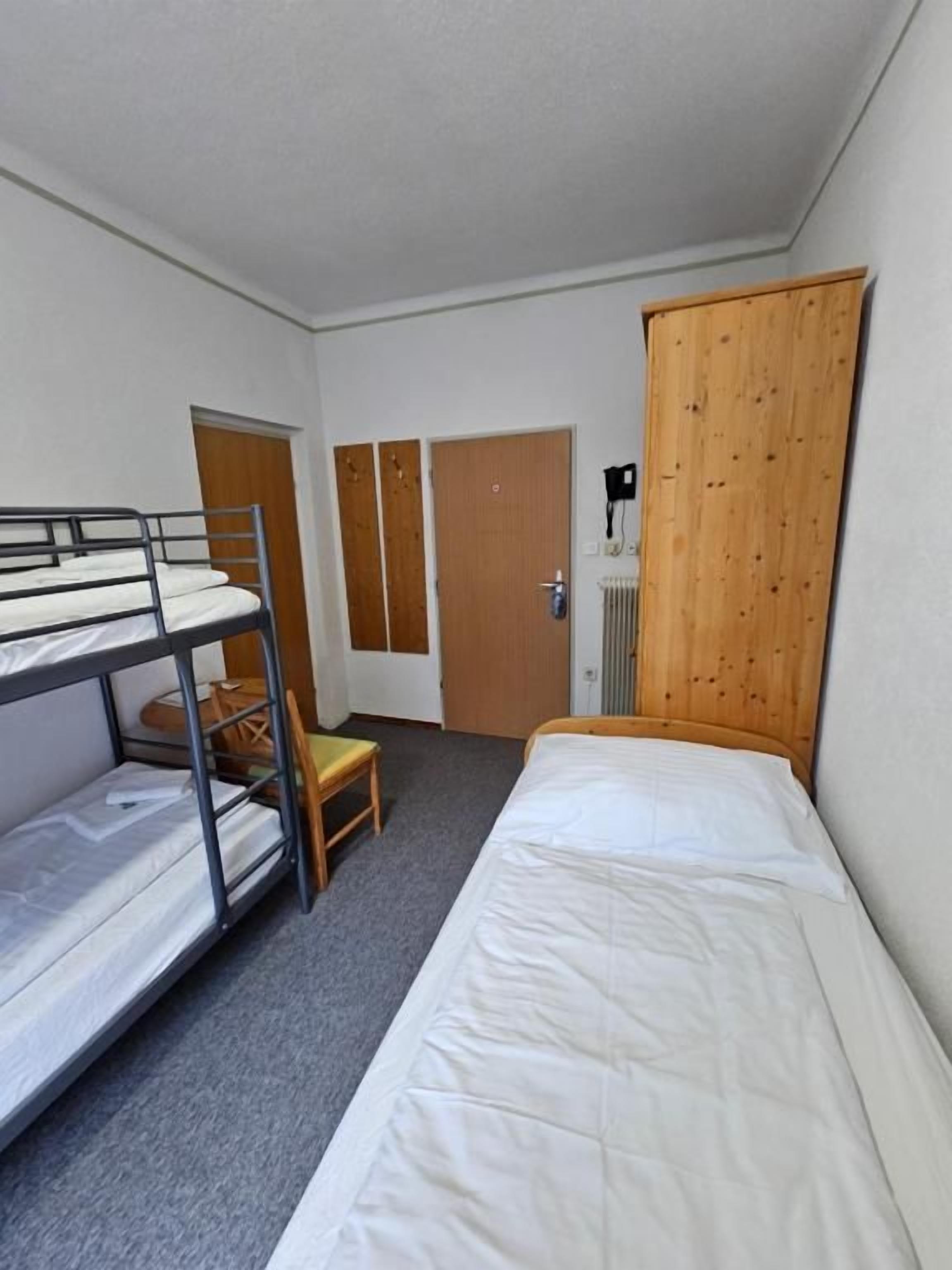 Un dormitorio con literas, una cama individual, un armario de madera y un radiador.