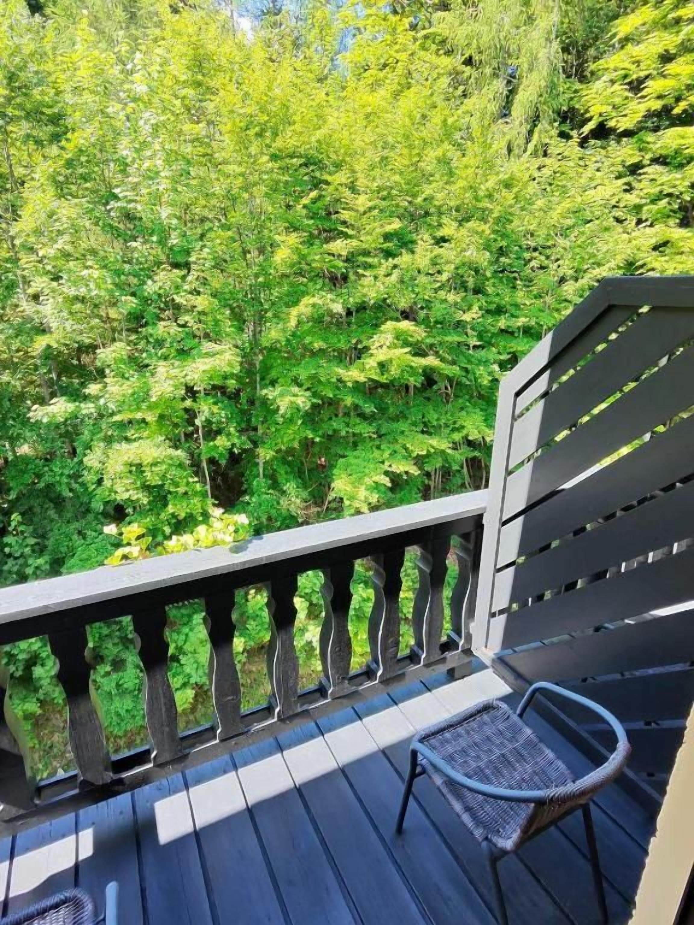 Una terraza de madera con una silla metálica y barandilla con vistas a un área boscosa.