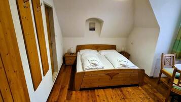 Un dormitorio con una cama de madera, una mesita de noche pequeña, una silla y una ventana con cortinas.