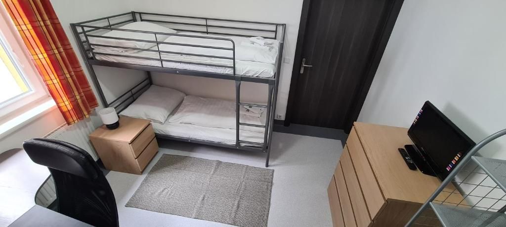Una cama litera con escritorio y silla, una computadora portátil en un estante y una ventana con cortinas.