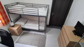 Una cama litera con escritorio y silla, una computadora portátil en un estante y una ventana con cortinas.