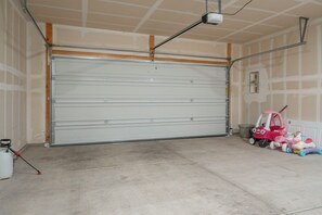 A garage with a closed metal door, a concrete floor, and a ceiling with exposed beams and a security camera. - Cozy 3BR Home in Tucson - Spacious Backyard + Great Location (Tucson)