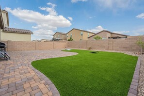 A backyard with artificial grass, a brick patio, and a brick wall. - Cozy 3BR Home in Tucson - Spacious Backyard + Great Location (Tucson)