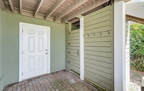 A covered porch with a white door, a brick floor, and a green wall with horizontal siding. - Oceanfront - Resort Access + Golf Cart (Fripp Island)