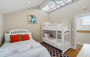 A bedroom with a bunk bed, a single bed with decorative pillows, a ceiling fan, a skylight, and a painting on the wall. - Oceanfront - Resort Access + Golf Cart (Fripp Island)