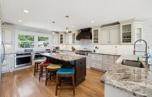 A spacious kitchen with white cabinetry, a large island with stools, and a view of the outdoors. - Oceanfront - Resort Access + Golf Cart (Fripp Island)